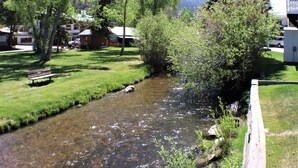 Un arroyo cristalino que serpentea por un espacio cubierto de hierba, con un banco de madera y una valla de madera.