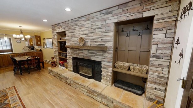 Una sala de estar con chimenea de piedra, un comedor con muebles de madera y una cocina al fondo.