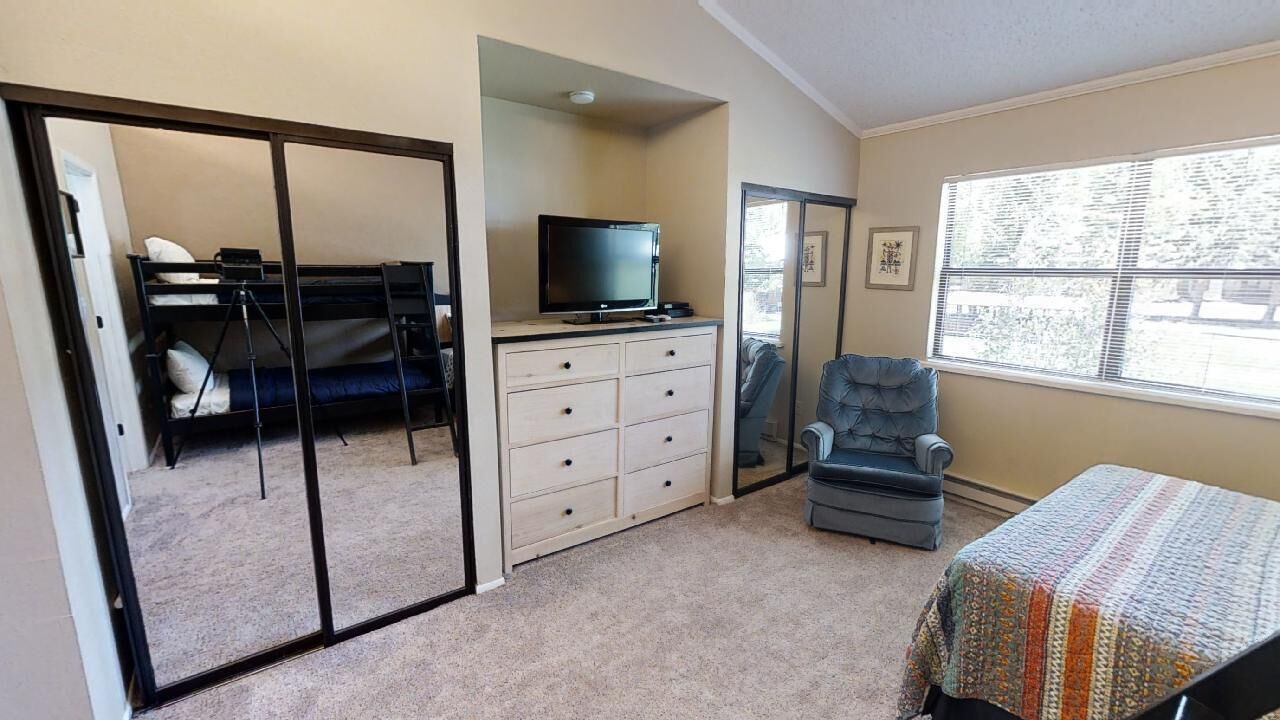 Un dormitorio con cama, cómoda, televisor, silla y ventana.