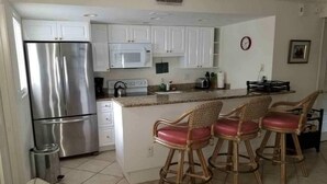 A kitchen with white cabinets, a stainless steel refrigerator, a microwave, and a coffee maker. There are three wicker bar stools with red cushions. - In the heart of Old Naples (Naples)