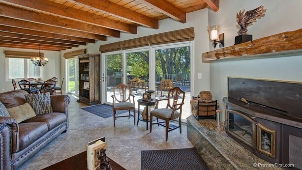 A spacious living room with a fireplace, wooden ceiling beams, and a dining area with outdoor views.