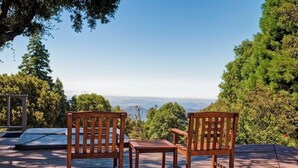 A wooden deck with two chairs and a table, overlooking a scenic view of mountains and trees.