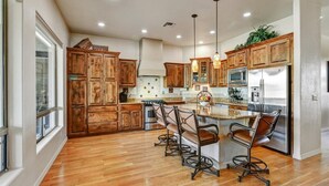 A spacious kitchen with wooden cabinets, a central island with bar stools, stainless steel appliances, and pendant lighting.