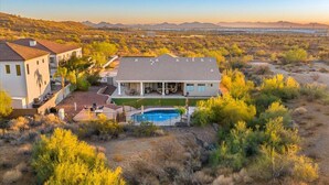 A large house with a swimming pool, surrounded by desert vegetation and mountains in the background.