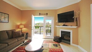Una sala de estar con sofá, mesa de centro, chimenea, televisor y puerta al balcón.