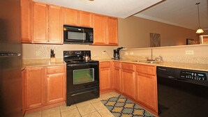 Una cocina con armarios de madera, microondas, estufa, lavavajillas y un tapete estampado.