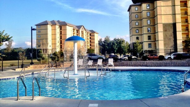 Piscina con sillas de descanso y una fuente de agua, rodeada de edificios de apartamentos.