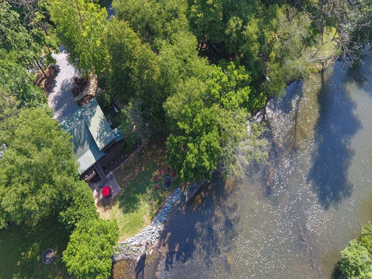 An aerial view of a house with a green roof, surrounded by dense greenery and a river.