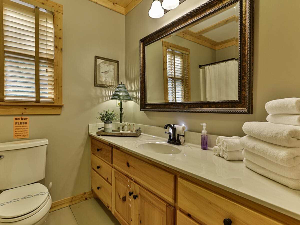 A bathroom with a wooden vanity, a large mirror, a toilet, and a stack of towels.
