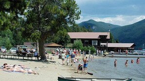 A beach with a row of boats, a building with a red roof, and mountains in the background. - Spacious Family Home In Town With Spectacular Lake And Mountain Views (Grand Lake)