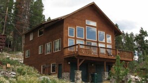 A two-story wooden cabin with a balcony, stone foundation, and multiple windows. - Spacious Family Home In Town With Spectacular Lake And Mountain Views (Grand Lake)