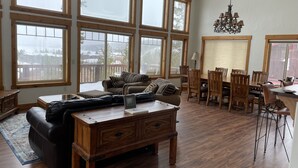 A spacious living room with a large wooden coffee table, a sofa with striped cushions, and a dining area with wooden chairs and a table. - Spacious Family Home In Town With Spectacular Lake And Mountain Views (Grand Lake)