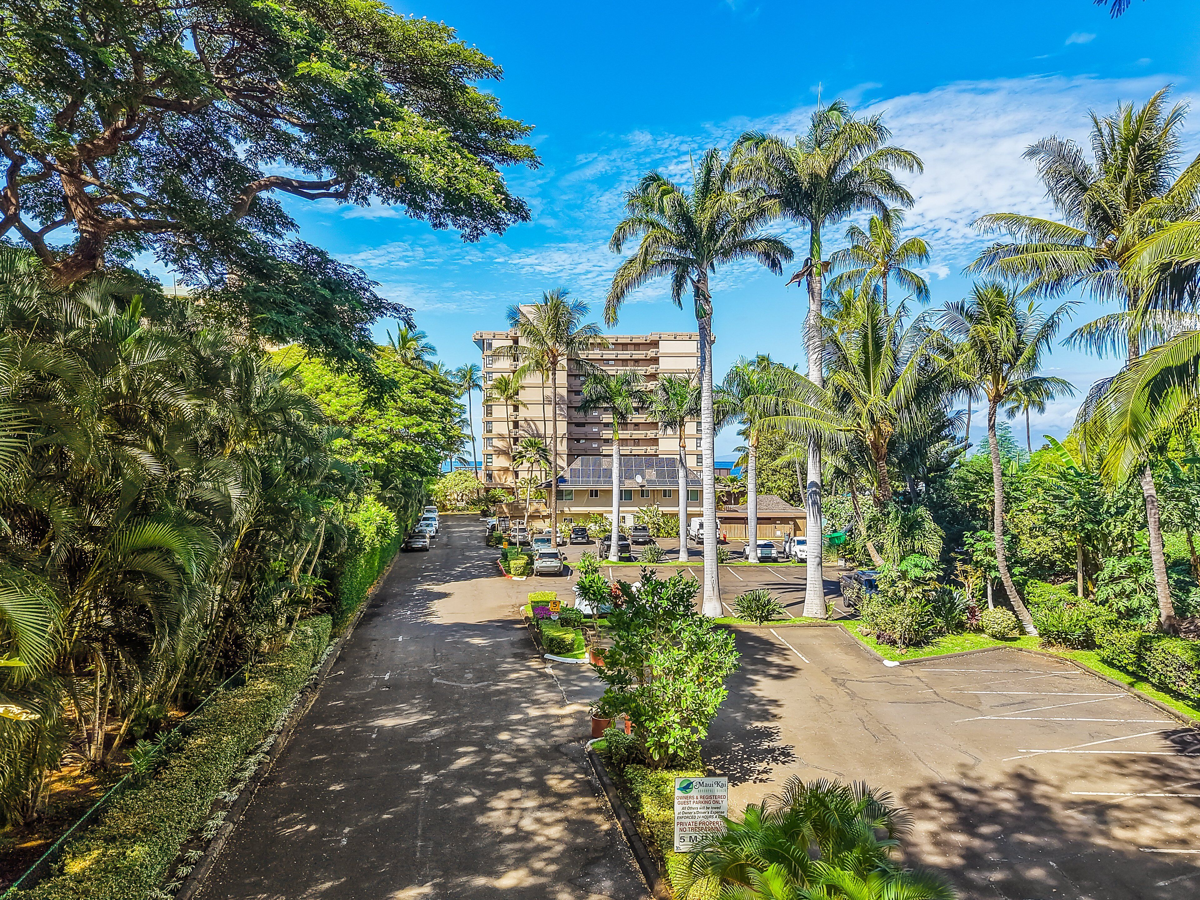 A hotel with a parking lot, surrounded by lush greenery and palm trees.