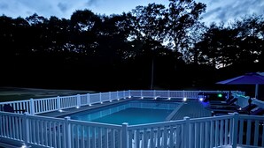 Une piscine rectangulaire dotée d’une plage et d’une rambarde blanches, entourée d’arbres.