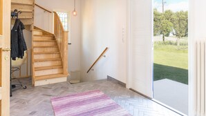 Une pièce spacieuse avec un escalier en bois, une grande porte-fenêtre coulissante donnant sur un jardin et un parquet à motifs en chevrons.