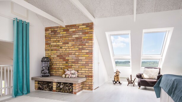 Une chambre avec une cheminée en briques, une grande fenêtre et une vue sur l’extérieur.