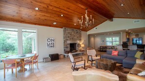 A spacious living room with a stone fireplace, wooden ceiling, and a dining area with a round table and chairs.