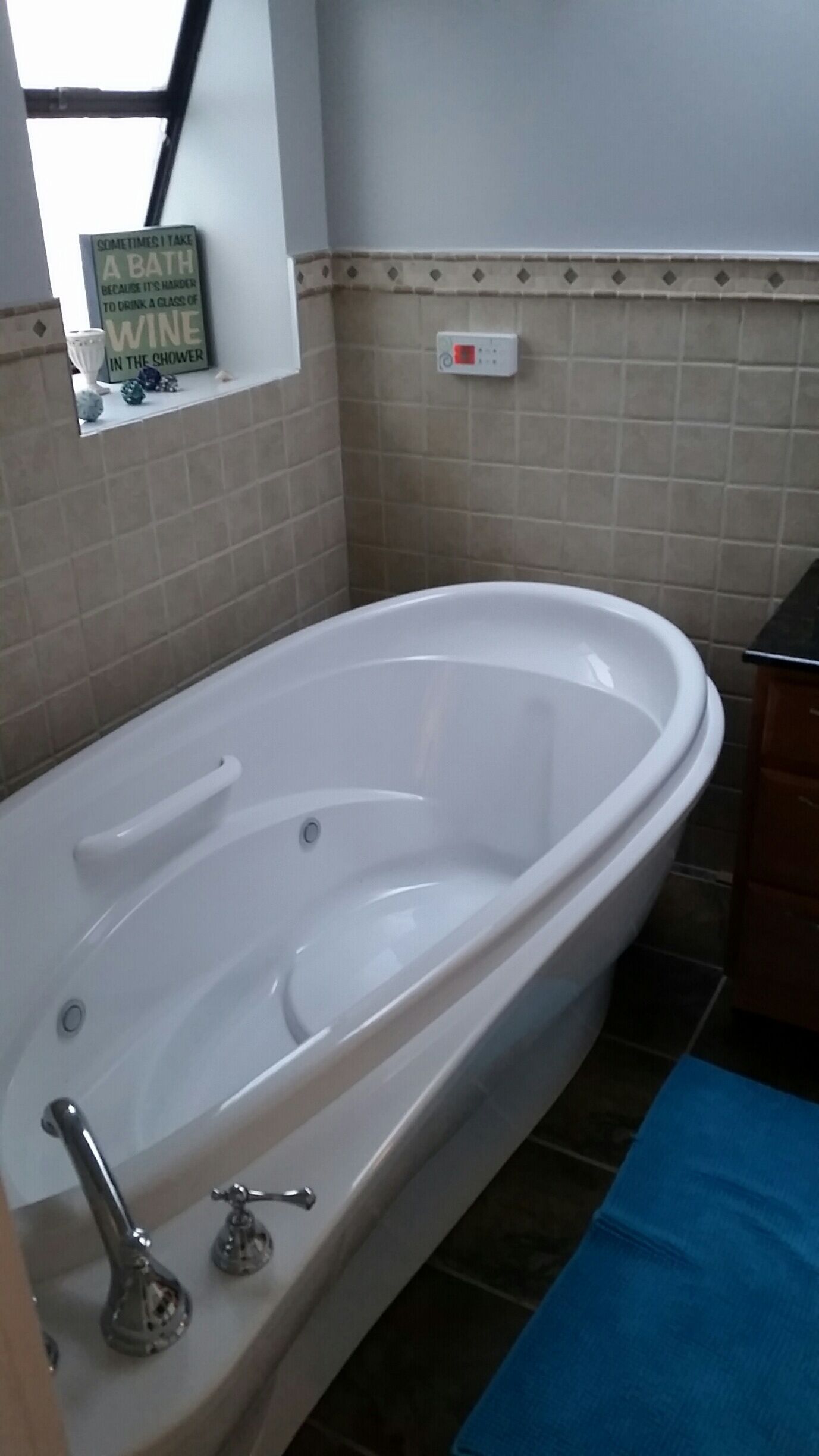 Une salle de bain avec une baignoire blanche, un porte-serviettes, un thermostat et un panneau sur le mur.