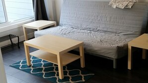A modern living room with a grey sofa, two wooden side tables, a blue patterned rug, and a dark wooden floor.