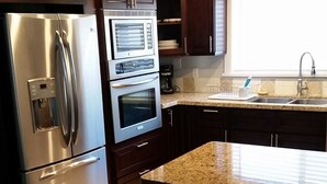 A modern kitchen with stainless steel appliances, dark wooden cabinets, and a granite countertop.