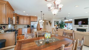 Una cocina amplia con armarios de madera, un comedor con mesa de vidrio y una sala de estar con chimenea y televisor.