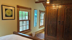 A bedroom with a large bed, wooden wardrobe, and two windows with views of the outdoors.