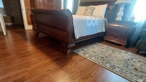 Quarto com piso de madeira, uma cama, mesa de cabeceira e cômoda.