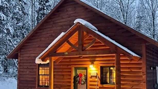 Een houten chalet met een sneeuwbedekte dak, een veranda met een groene deur, en een klein raam aan de zijkant.