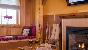 Een gezellig chaletinterieur met een houten bank, een open haard en een raam met bloemen.