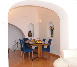Een eethoek met een houten tafel, blauwe stoelen en een bloevas aan de muur.