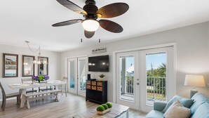 A spacious living room with a dining area, a ceiling fan, a flat-screen TV, and a balcony with a view. - Gulf Place Caribbean - Top Rated Condo on 30-A with Pickleball & Tennis! (Santa Rosa Beach)