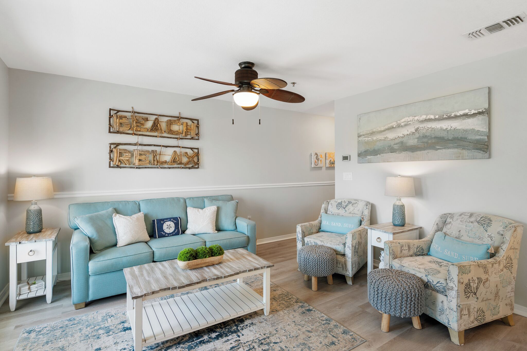 A living room with a blue sofa, a patterned armchair, a coffee table, and a ceiling fan.