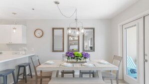 A dining area with a white table, blue chairs, and a bench. There are two mirrors on the wall, a clock, and a chandelier. - Gulf Place Caribbean - Top Rated Condo on 30-A with Pickleball & Tennis! (Santa Rosa Beach)