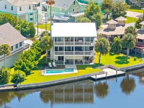 A multi-story building with a pool, surrounded by greenery and a water body.
