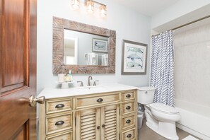 A bathroom with a wooden vanity, a white sink, a mirror, a toilet, and a shower curtain. - Eagle Nest/Your Private Waterfront Escape on Florida's Nature Coast. (Hernando Beach)