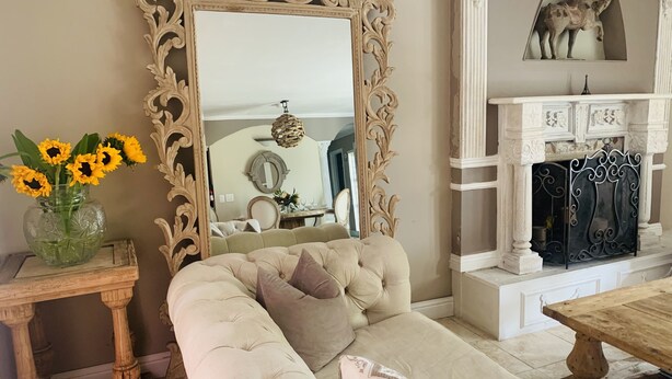 A living room with a large ornate mirror, a beige sofa with cushions, a wooden coffee table, and a vase with sunflowers. - Beautiful Spanish style home- Garden. Fremont, California.  (Fremont)