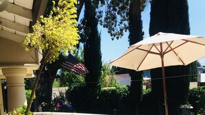 An outdoor patio with a beige sofa, a table, and an umbrella. There are plants and a railing around the patio. - Beautiful Spanish style home- Garden. Fremont, California.  (Fremont)