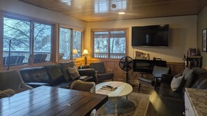 A cozy living room with a wooden ceiling, large windows, a flat-screen TV, and a fireplace. - Whole lodge can sleep 30! Great family getaway. Exempt motor permit available.  (Grand Marais)