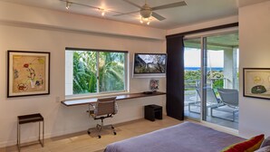 Une chambre moderne avec un grand lit, un bureau, une chaise et un téléviseur. Elle dispose d’un balcon avec vue sur l’océan.