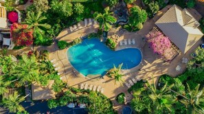 An aerial view of a resort with a large swimming pool surrounded by palm trees and lounge chairs.