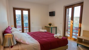 A bedroom with a bed, a bedside table with a lamp, a small table with a flower, and a TV on the wall. - Il Moscardino Country Resort (Serra San Bruno)