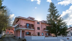 A pink multi-story building with balconies, a paved courtyard, and a large tree. - Il Moscardino Country Resort (Serra San Bruno)