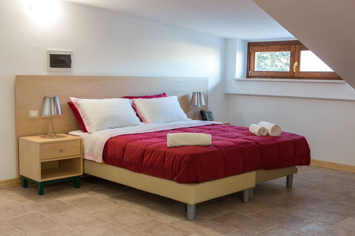 Un dormitorio con cama, mesitas de noche, ventana y termostato.