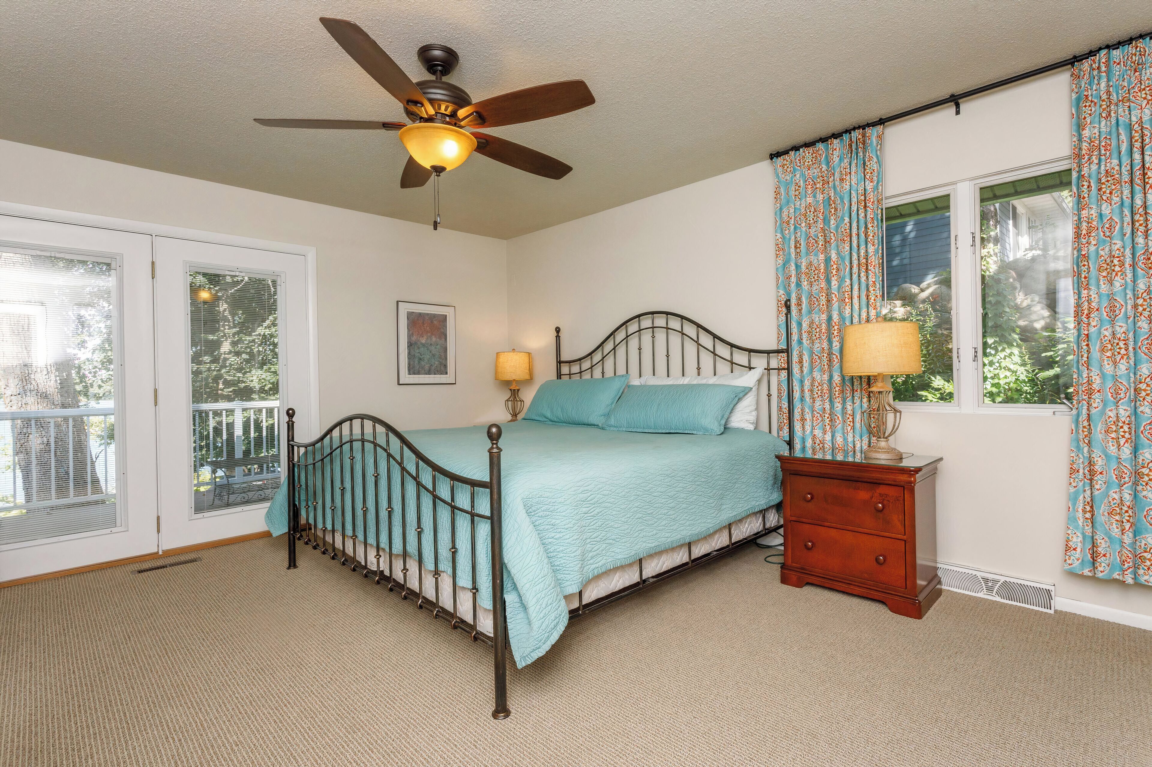 A bedroom with a bed, a nightstand, a ceiling fan, and a window with curtains.