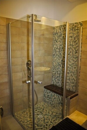 Enjoy a refreshing shower in this modern bathroom with a glass-enclosed stall, shelf, and mosaic-tiled walls.
