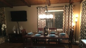 A dining area with a wooden table set for four, surrounded by chairs. A stone wall and a flat-screen TV are visible in the background. - Beautifully Renovated South Lake Tahoe Condo  Minutes To Casinos, Ski & Beaches (Zephyr Cove)