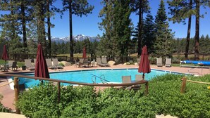 A pool area with lounge chairs and umbrellas, surrounded by greenery and a mountain backdrop. - Beautifully Renovated South Lake Tahoe Condo  Minutes To Casinos, Ski & Beaches (Zephyr Cove)