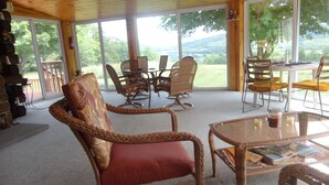 A room with wicker furniture, a glass table, and large windows offering a view of the outdoors.