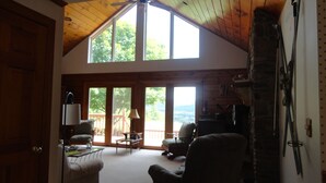A spacious living area with a high ceiling, large windows, and a stone fireplace.