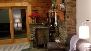 A cozy living room with a stone fireplace, a brown leather sofa, and a wooden floor.